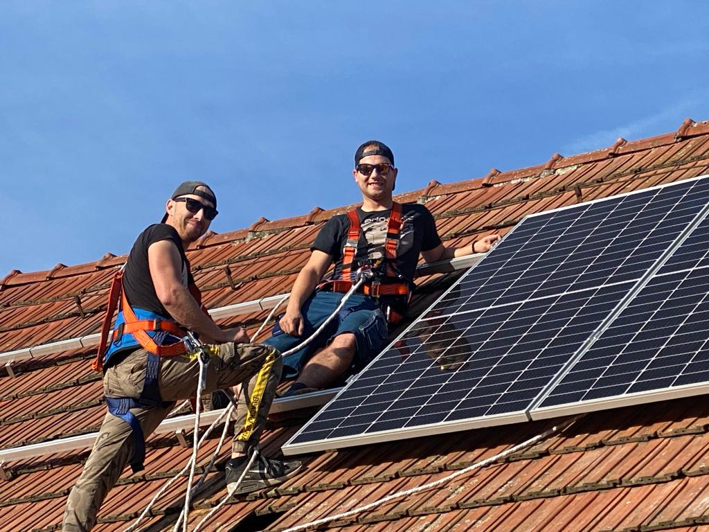 Dva montážníci s jištěním osazují fotovoltaické panely na střeše