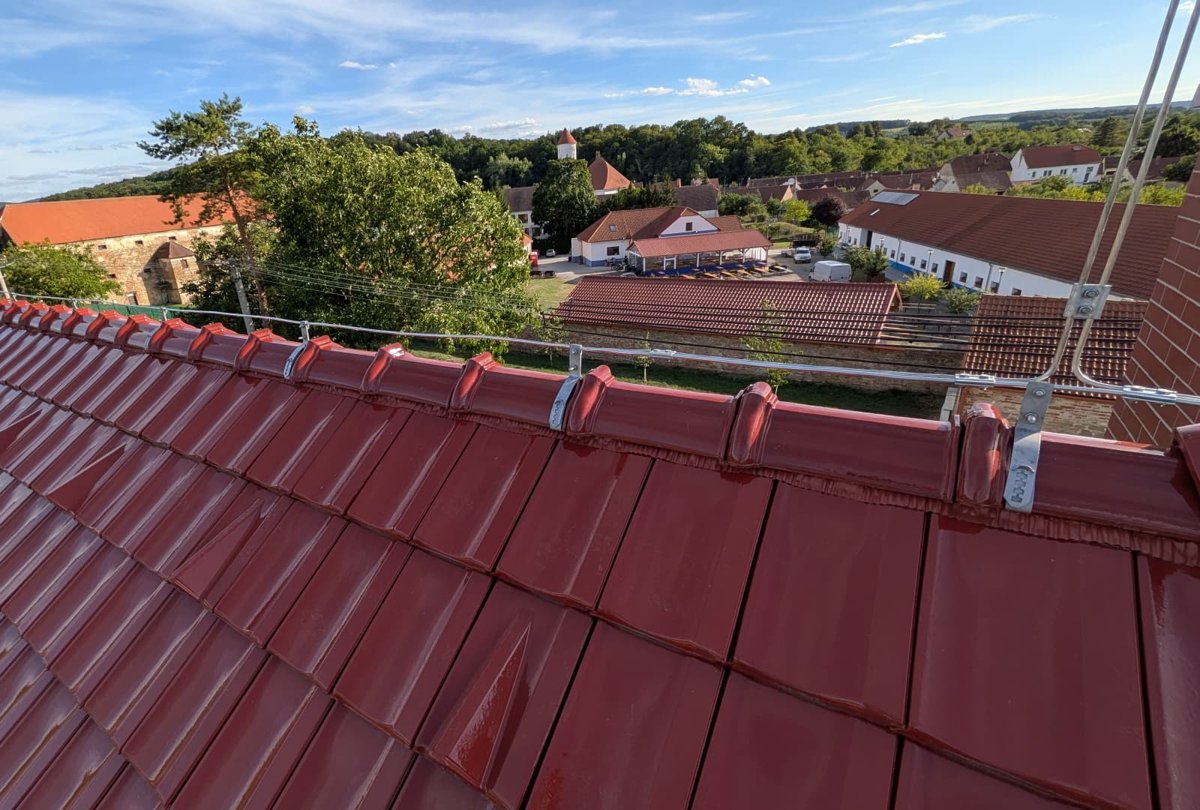 Jímací vedení hromosvodu v držácích na hřebeni červené taškové střechy